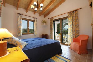 A bedroom with a bed, a chair, a lamp, a window, and a view of the outdoors.