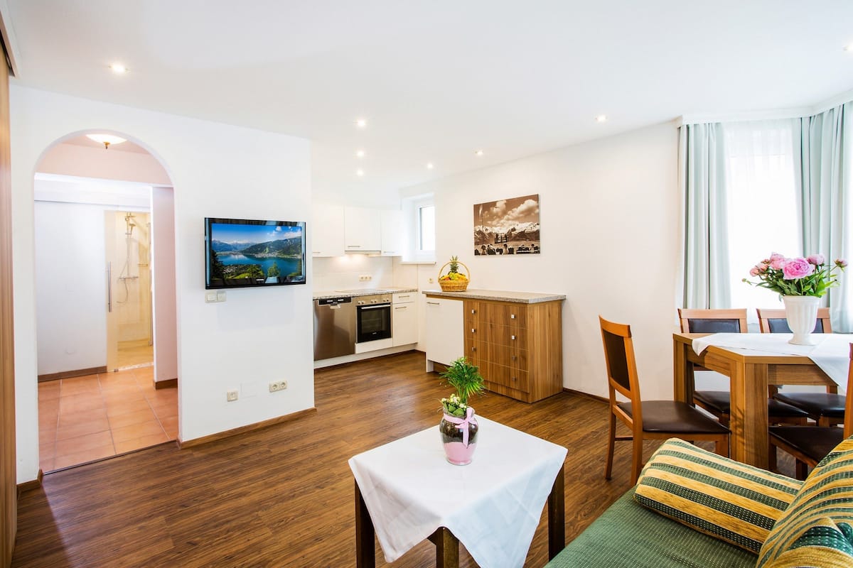 A modern living room with a dining area, kitchen, and a TV mounted on the wall.