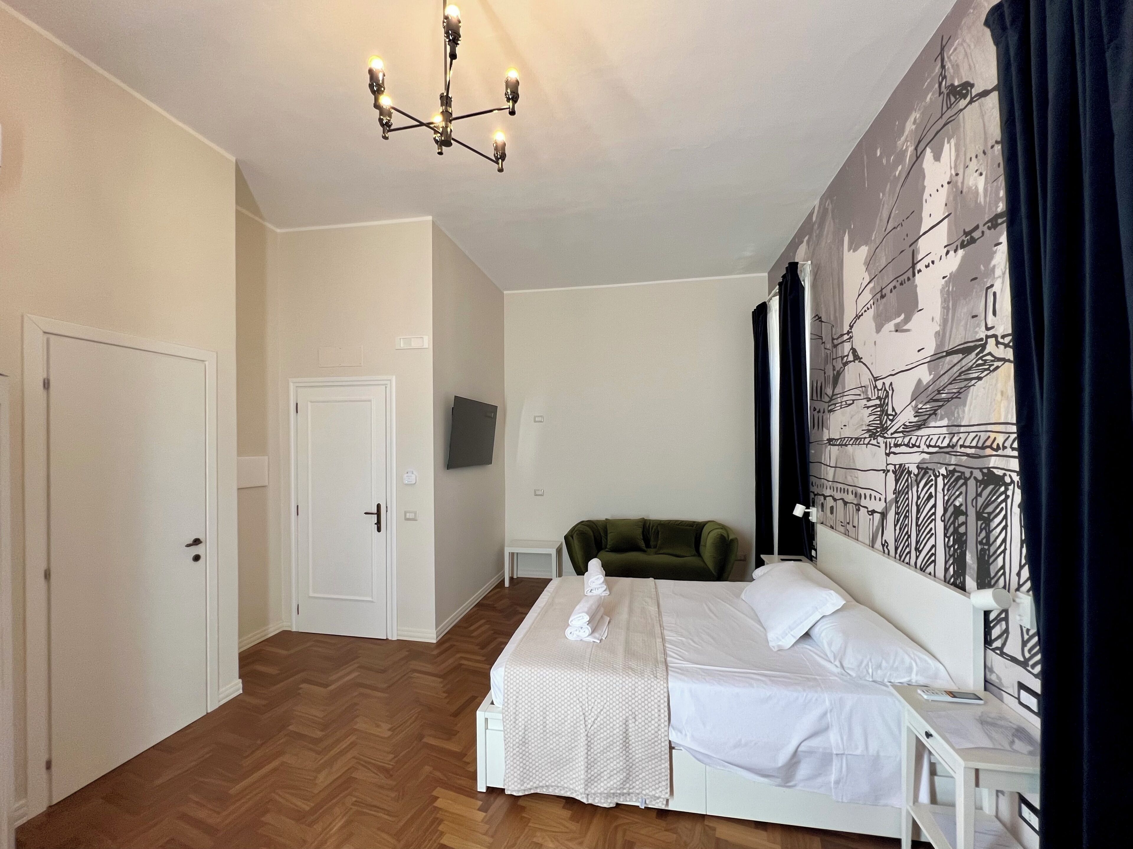 Een slaapkamer met een bed, een groene stoel, een televisie en een groot wandtapijt.