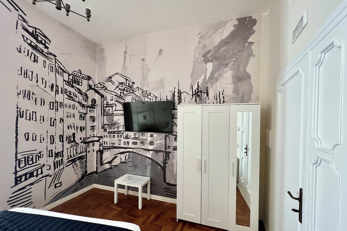 Een slaapkamer met stadsgezicht muurschildering, een bed, een klein tafeltje en een kledingkast.