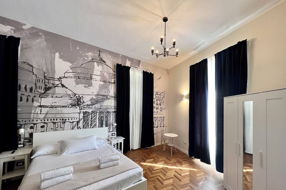 Een slaapkamer met een bed, nachtkastje, stoel, kledingkast en een muurschildering.