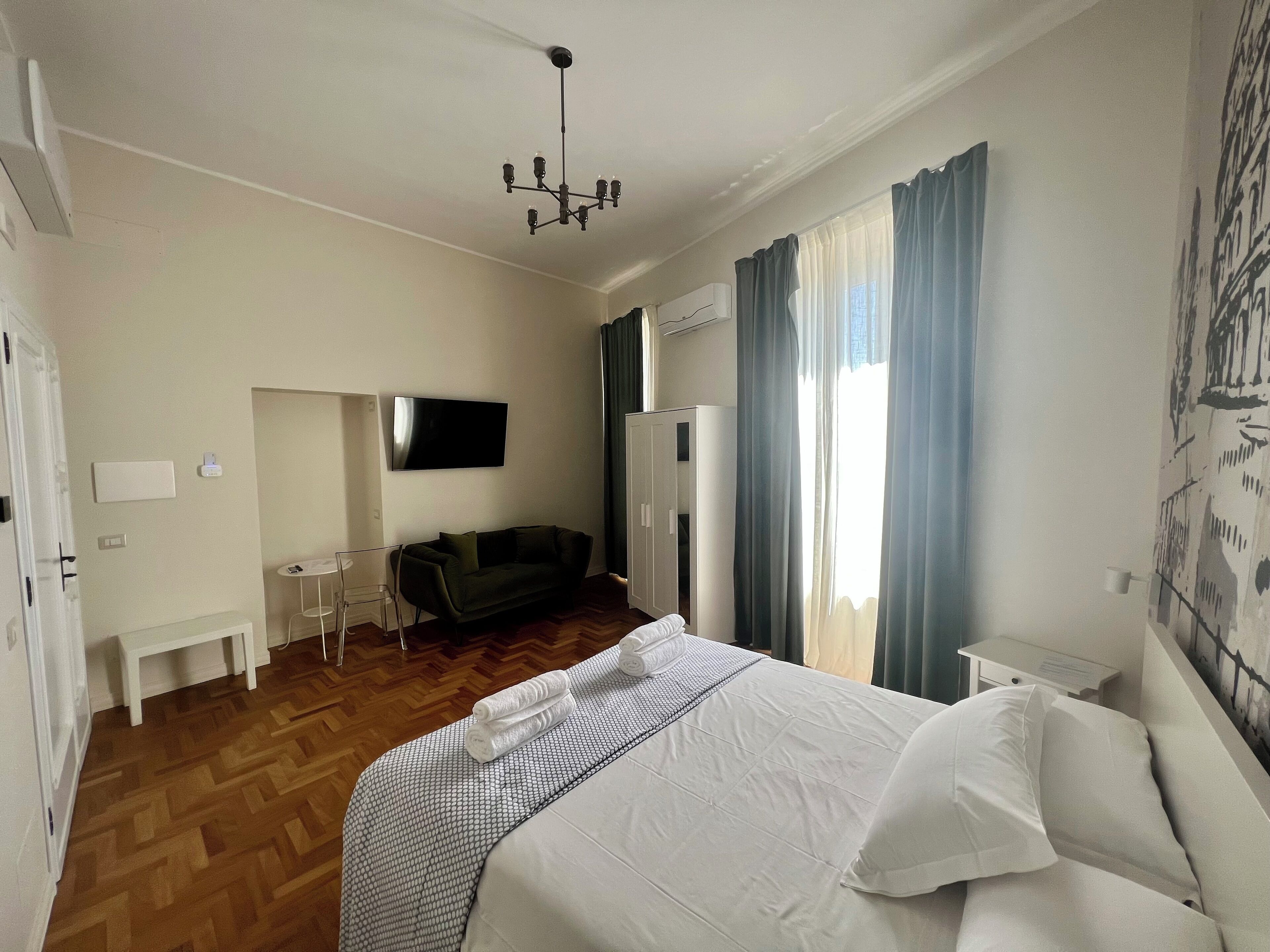 Ein Hotelzimmer mit einem Bett, einem an der Wand montierten Fernseher, einem Schreibtisch, einem Stuhl und einem Kleiderschrank.
