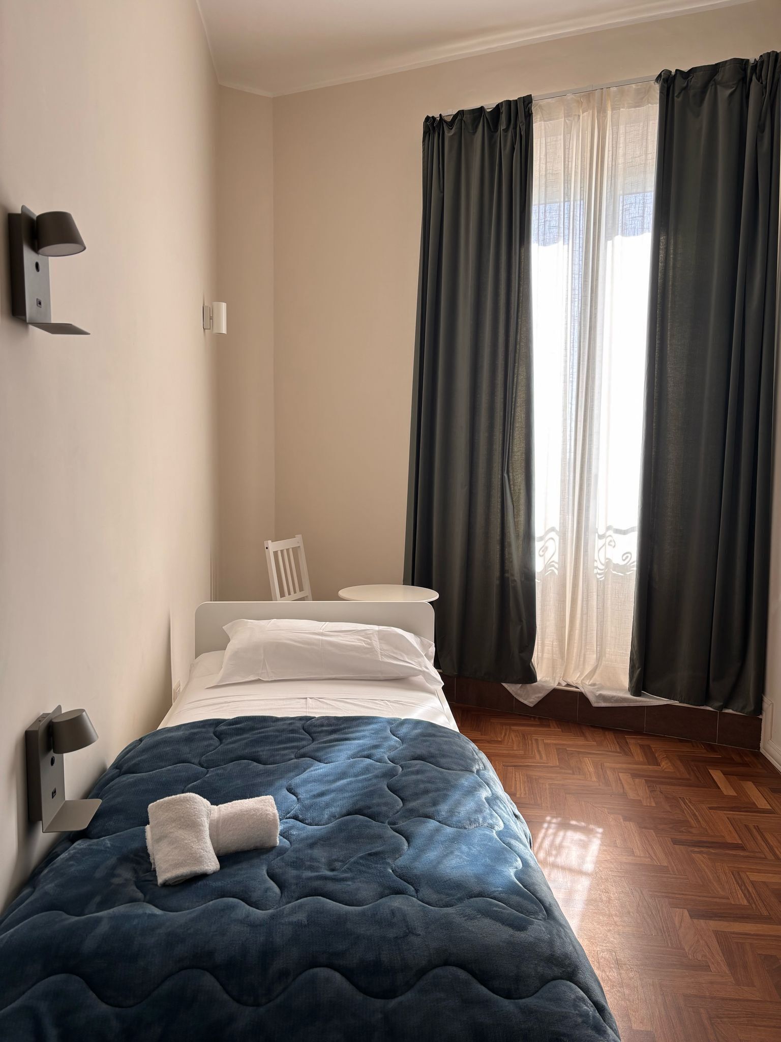 A bedroom with a bed, a chair, a nightstand, and a window with curtains.