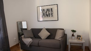 Ein Wohnzimmer mit grauem Sofa, einem kleinen weißen Beistelltisch und einem gerahmten Kunstwerk an der Wand.