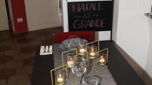 A dining table set with candles, plates, and cutlery, with a sign reading "NATALE del GRANDE" on the wall. - Home2Rome - Trastevere Del Grande (Rome)