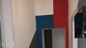 A living room with a black sofa, a dining table with chairs, and a red and blue accent wall. - Home2Rome - Trastevere Del Grande (Rome)