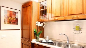 A kitchen with wooden cabinets, a stainless steel sink, and a framed artwork on the wall. - Home2Rome - Trastevere Roma Libera (Rome)