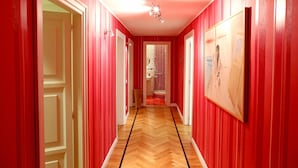 A hallway with red walls and a wooden floor, leading to a bathroom with a sink and toilet. - Home2Rome - Trastevere Roma Libera (Rome)