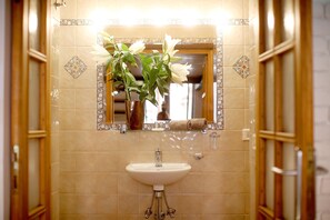 A bathroom with a white sink, a mirror, and a vase with white flowers.