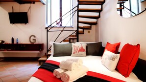 A bedroom with a bed, pillows, a red and black bedspread, a TV on the wall, and a staircase. - Home2Rome - Trastevere Galletti (Rome)