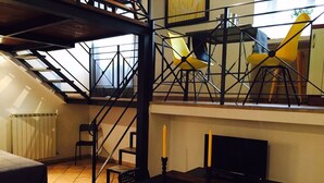 A loft-style room with a sloped ceiling, a wooden table, a black TV, and a yellow chair. - Home2Rome - Trastevere Mercanti I (Rome)