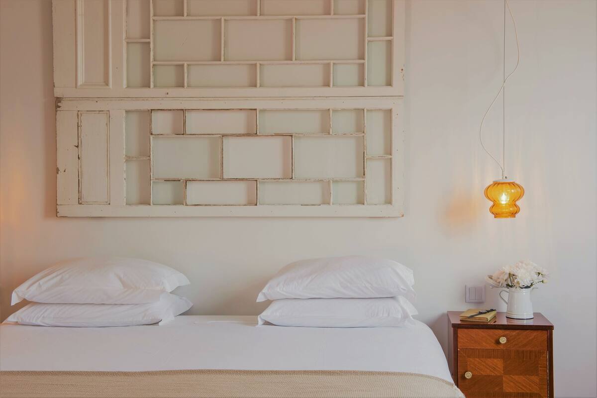A bedroom with a bed, two pillows, a nightstand with a lamp, and a wall-mounted light fixture.