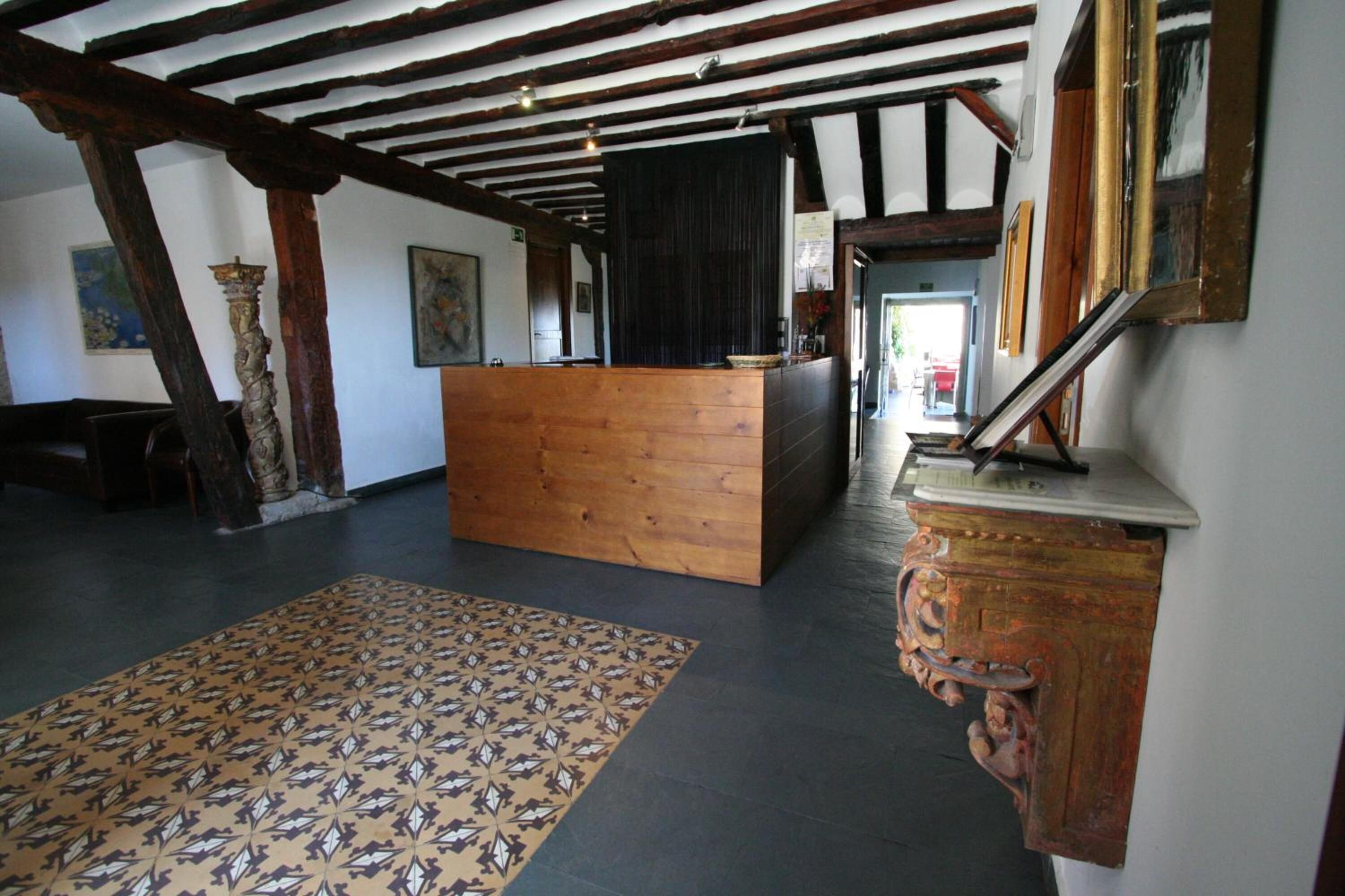 Une pièce avec des poutres apparentes, un tapis à motifs, un comptoir d’accueil en bois et un miroir au mur.