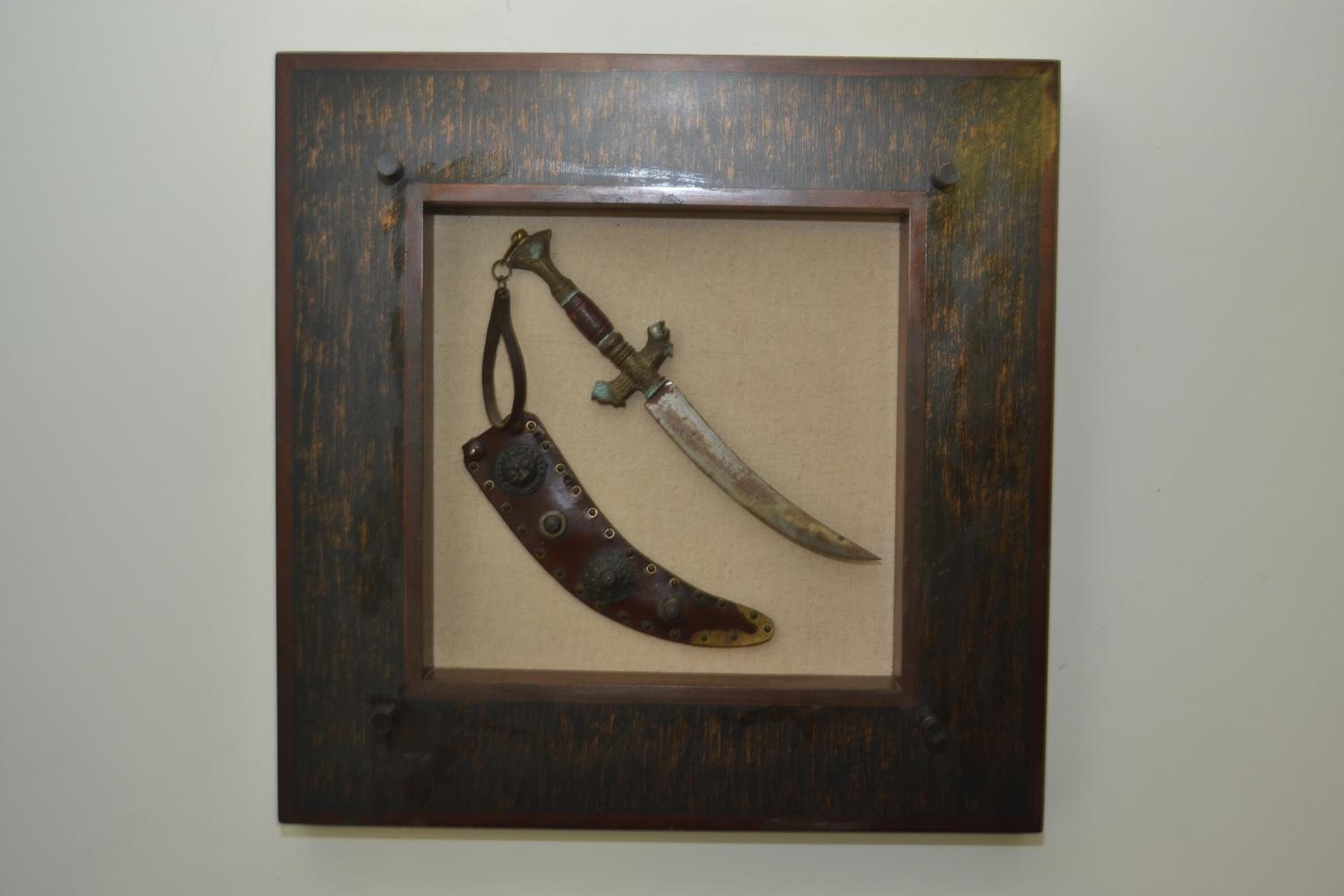 A framed display of a knife and a curved blade with a leather sheath.