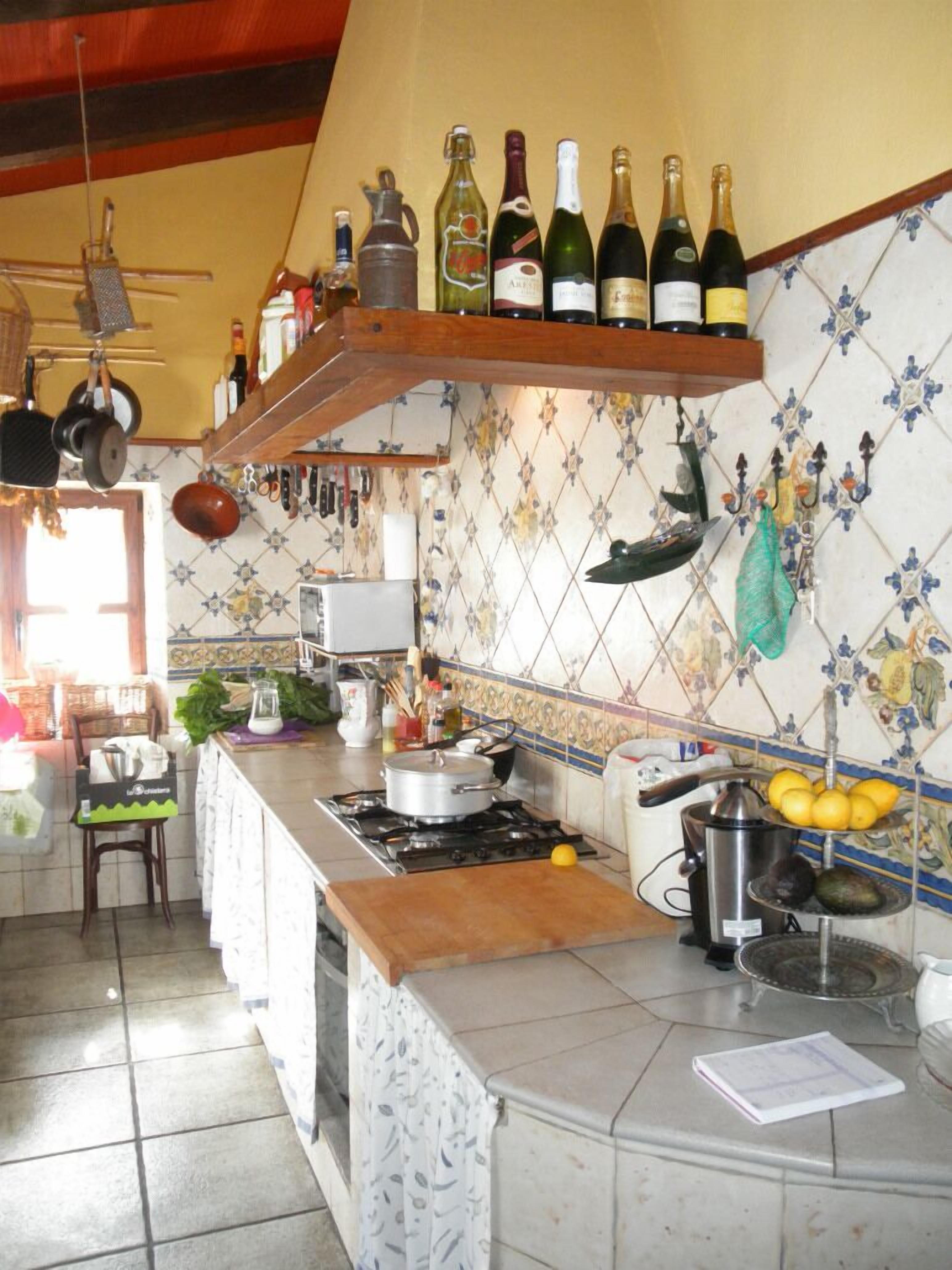 A kitchen with a stove, a sink, and various cooking utensils. There are bottles of wine on a shelf above the stove.