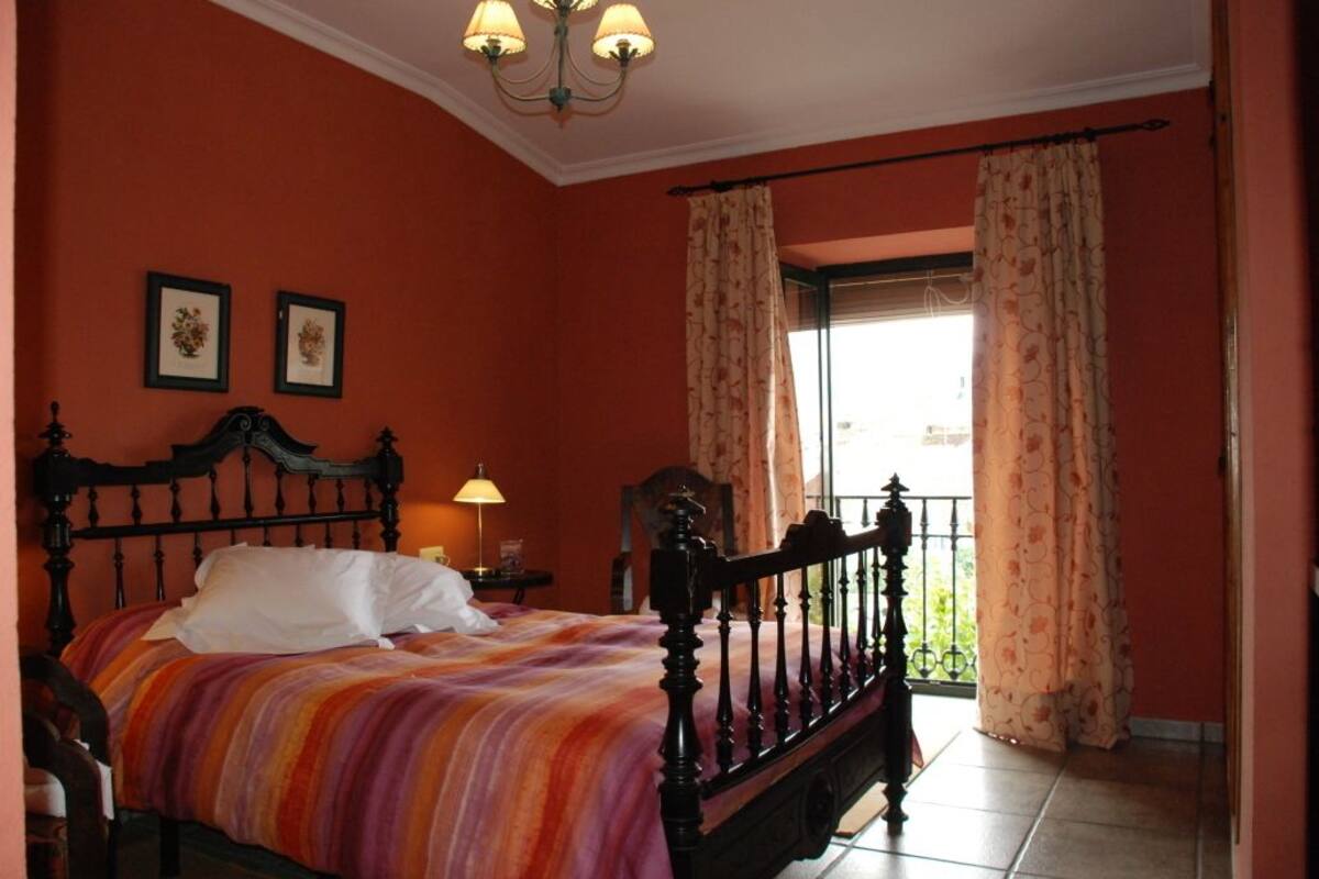 Une chambre à coucher avec un lit, une table de chevet, une lampe et une fenêtre avec des rideaux.