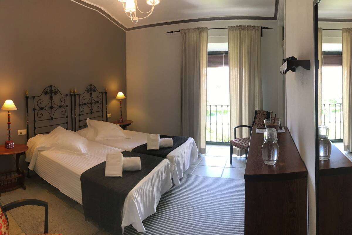 Une chambre d’hôtel avec deux lits, une petite table sur laquelle se trouve un vase, une chaise et une vue sur le balcon extérieur.