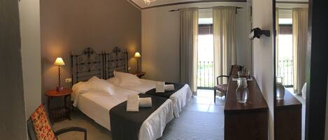 Ein Hotelzimmer mit zwei Betten, einem kleinen Tisch mit einer Vase, einem Sessel und Blick auf den Balkon.