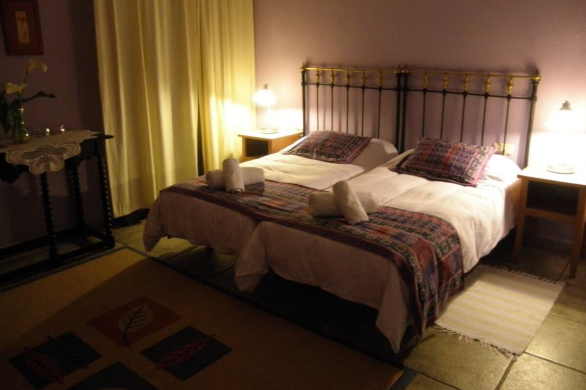Un lit double avec une tête de lit en métal, deux tables de chevet avec des lampes, une table de chevet ornée d’un vase de fleurs et un tapis à motifs.