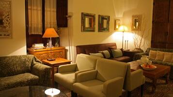 Una sala de estar acogedora con un sofá estampado, un sillón verde, una mesa de centro de madera y una lámpara.