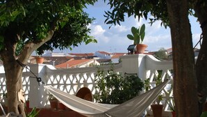 Un hamac suspendu sous une structure en treillis blanc, agrémentée de plantes en pot, avec vue sur des bâtiments.