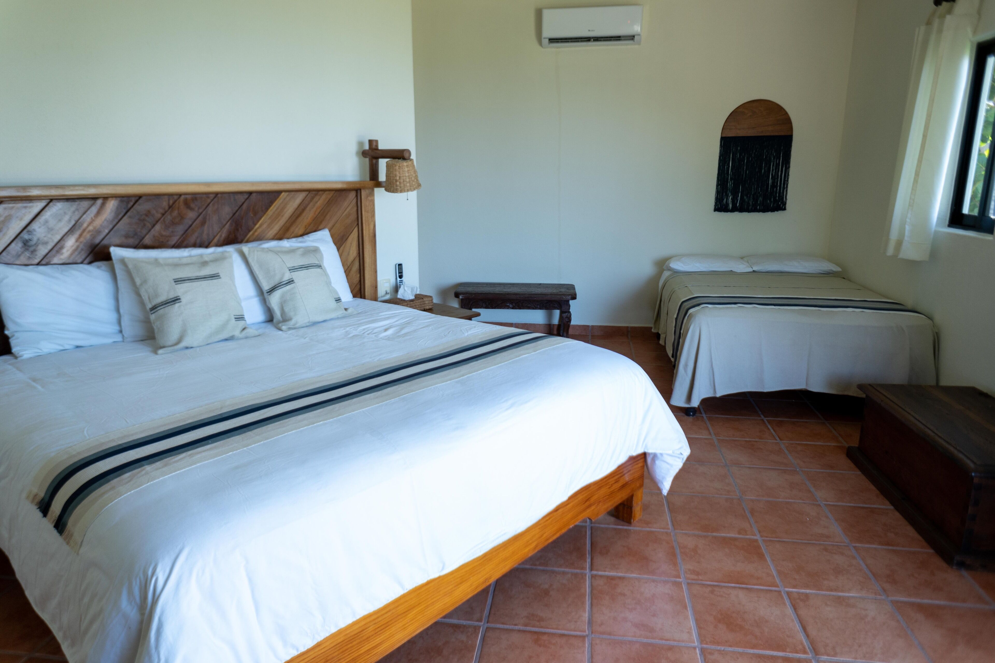 A bedroom with a large bed, two smaller beds, a wooden headboard, a bench, and a small table.