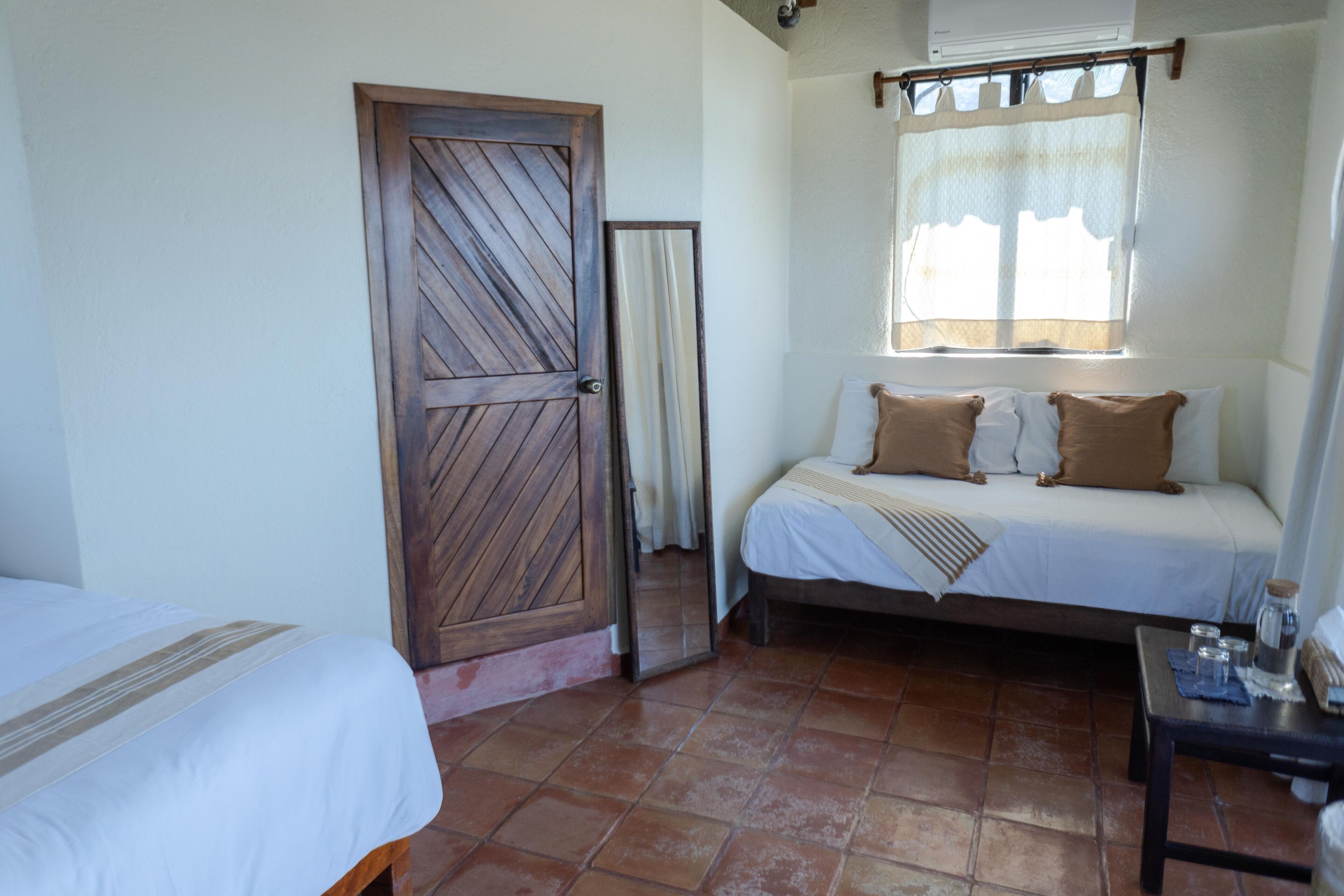 Un dormitorio con cama, mesita de noche, ventana con cortinas y puerta.