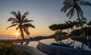 Vista de la piscina al atardecer, con palmeras y cielo despejado.