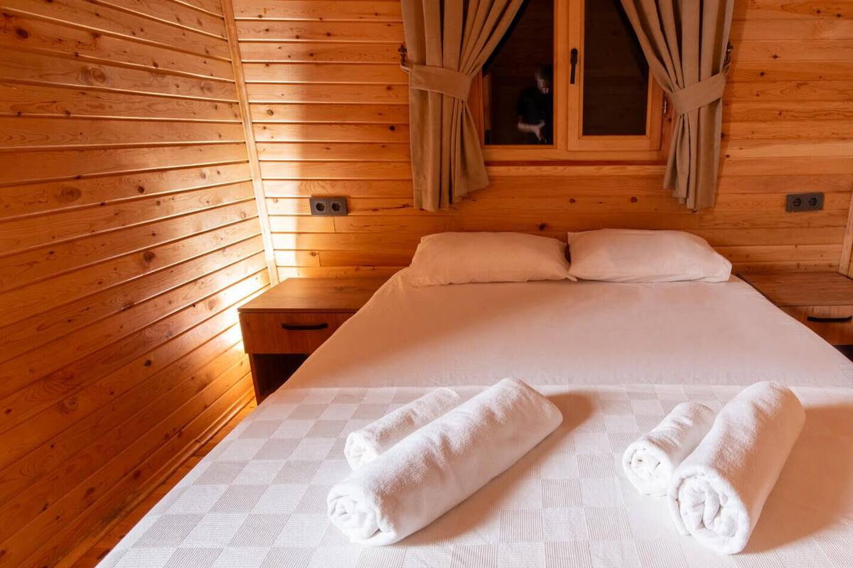 A wooden cabin room with a bed, two nightstands, and a window with curtains.
