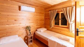 Una habitación de cabaña de madera con dos camas individuales, una mesita con un florero y una ventana con cortinas.
