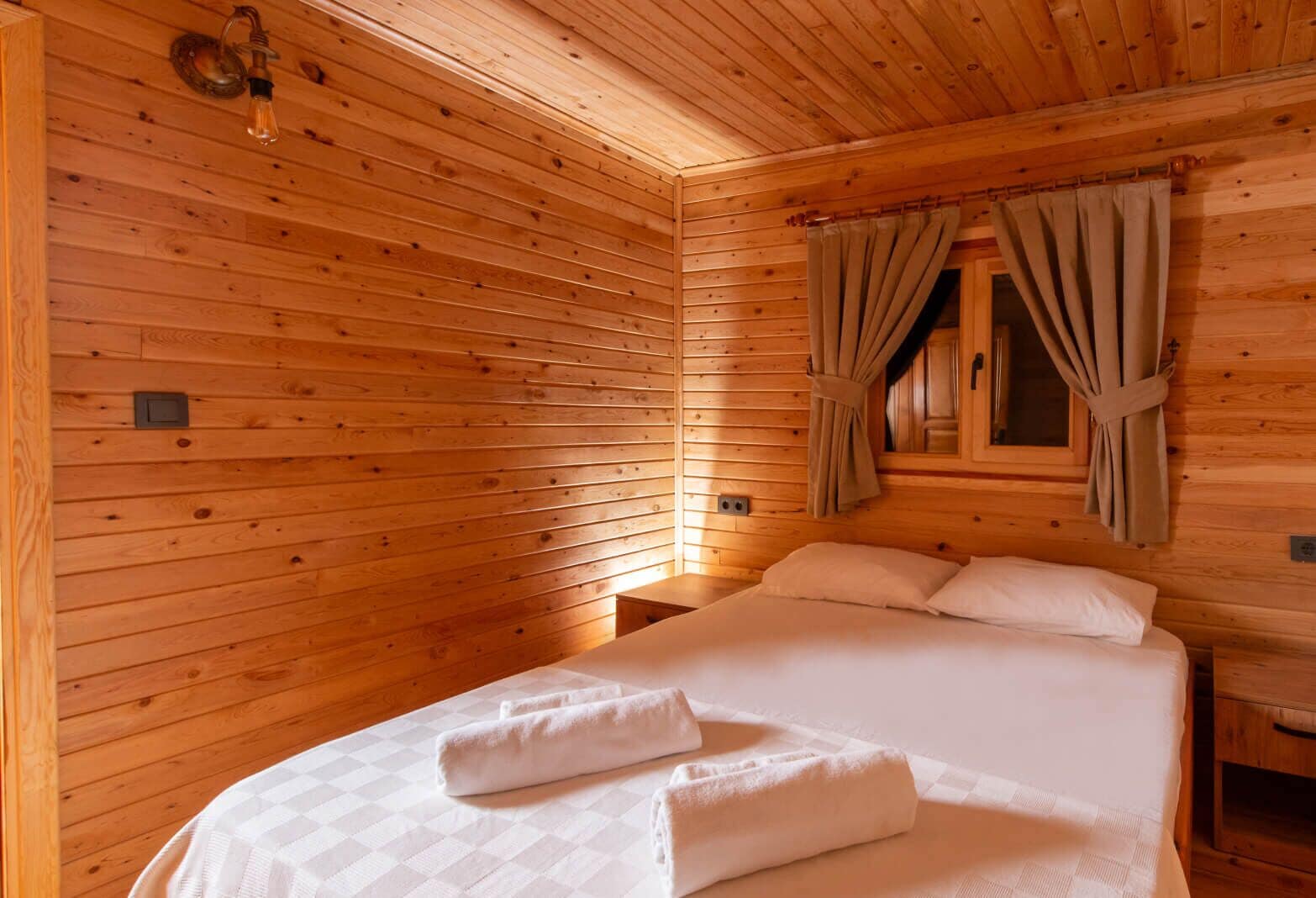Una habitación de cabaña de madera con cama, cortinas y ventana.