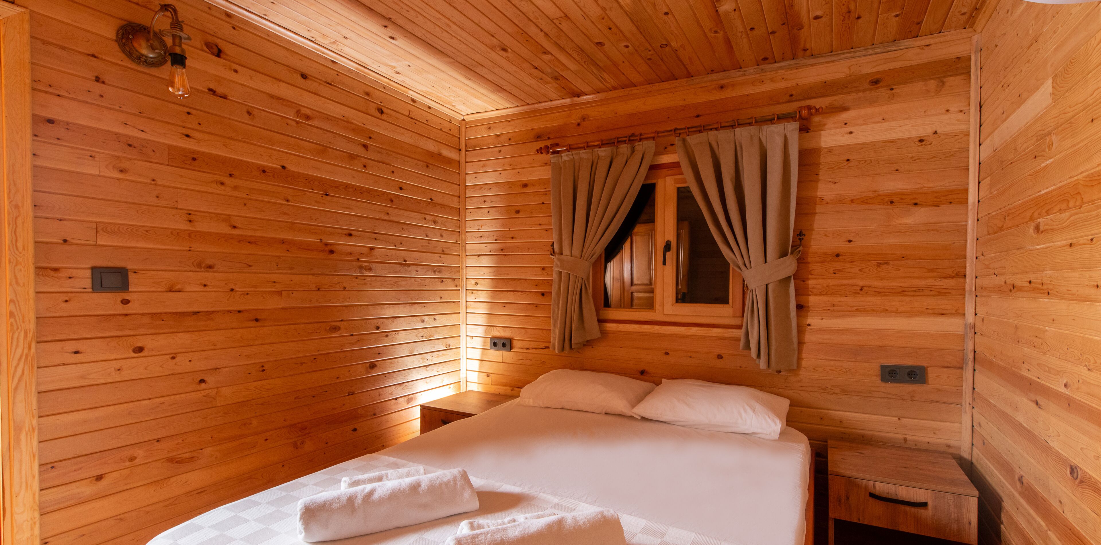 A wooden cabin room with a bed, curtains, and a window.
