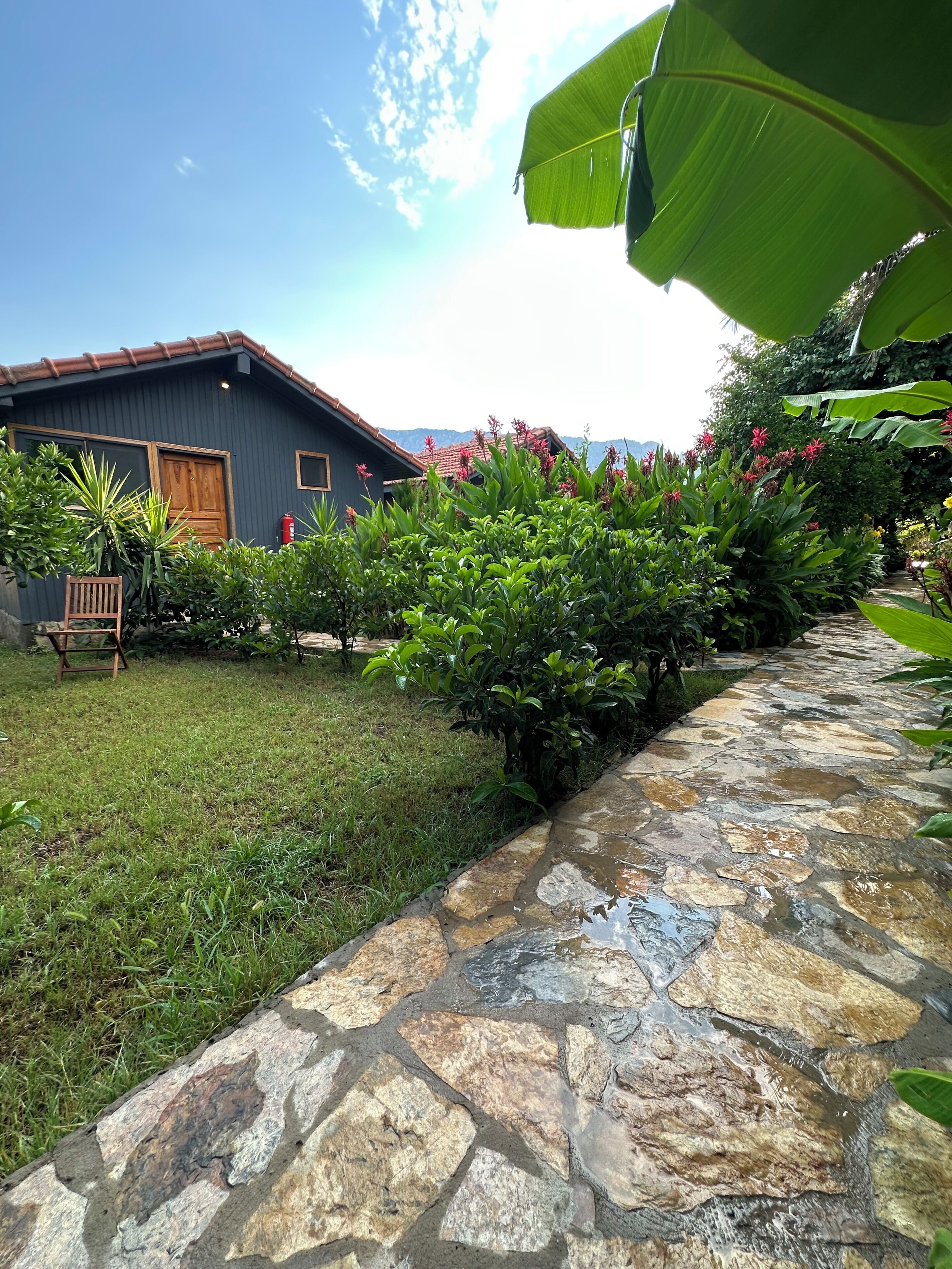Uma trilha de pedras que leva a uma casa com fachada escura e telhado em telhas.
