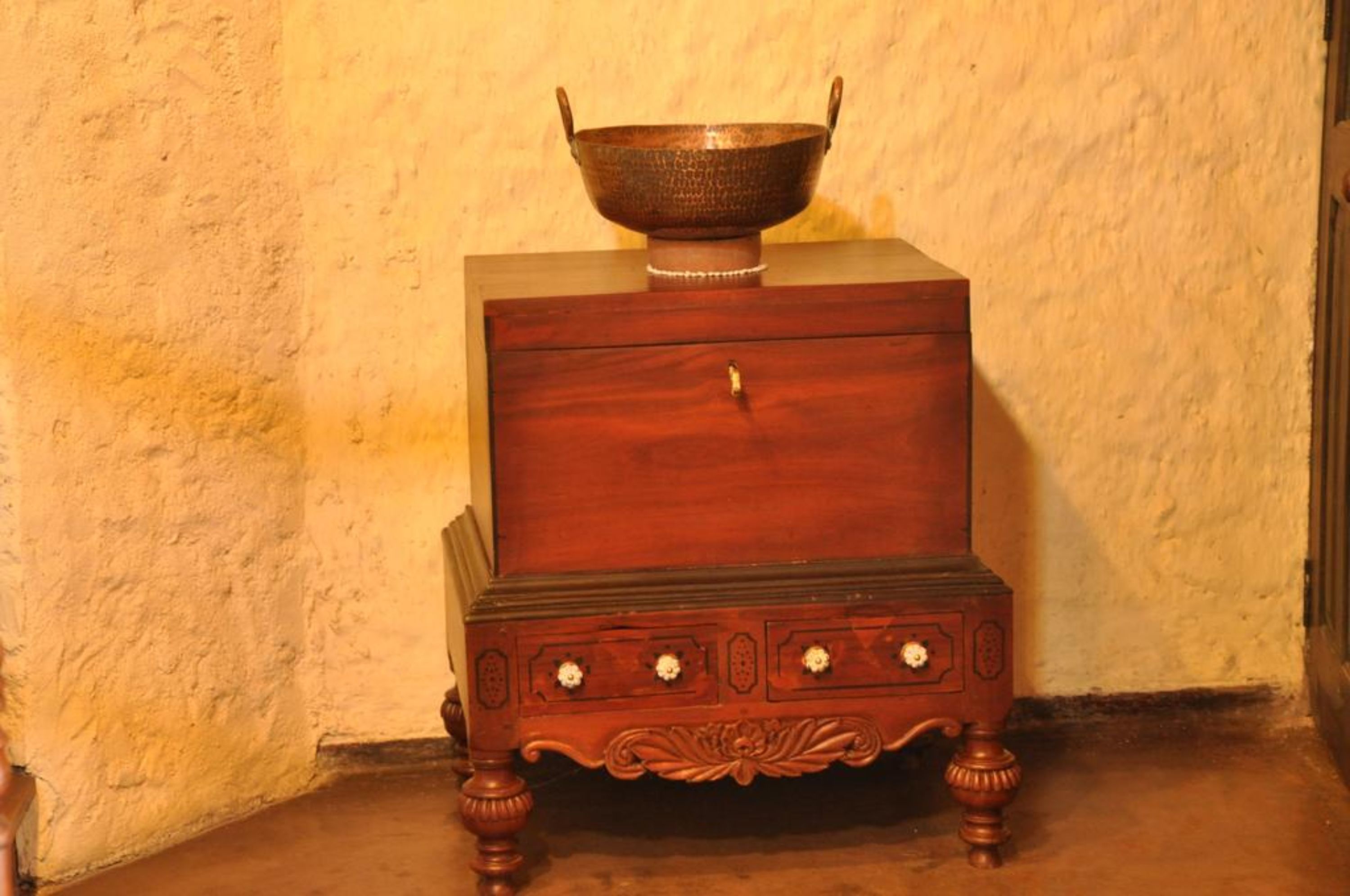 Una estufa de madera con un tazón metálico encima, apoyada contra una pared con textura.