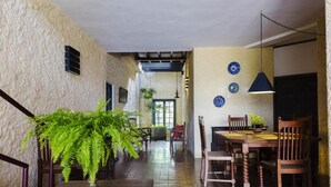 Uma sala de jantar com mesa e cadeiras de madeira, luminária pendente e planta em vaso.