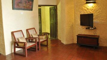 Una habitación con dos sillas de madera, una mesa pequeña, un televisor montado en la pared y una puerta que da a otra estancia.