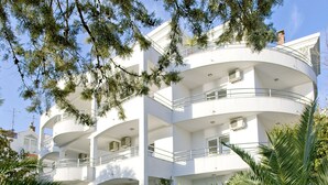 Un immeuble blanc à plusieurs étages, doté de balcons et entouré de plantes tropicales.