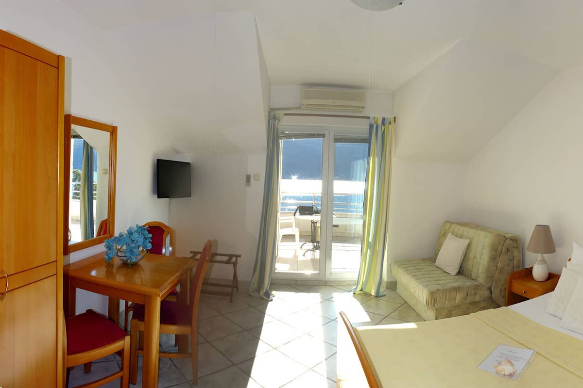 Habitación de hotel con cama, mesitas de noche, escritorio con silla, televisor y balcón con vistas.