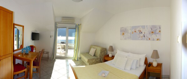 A hotel room with a bed, bedside tables, a desk with a chair, a television, and a balcony with a view.