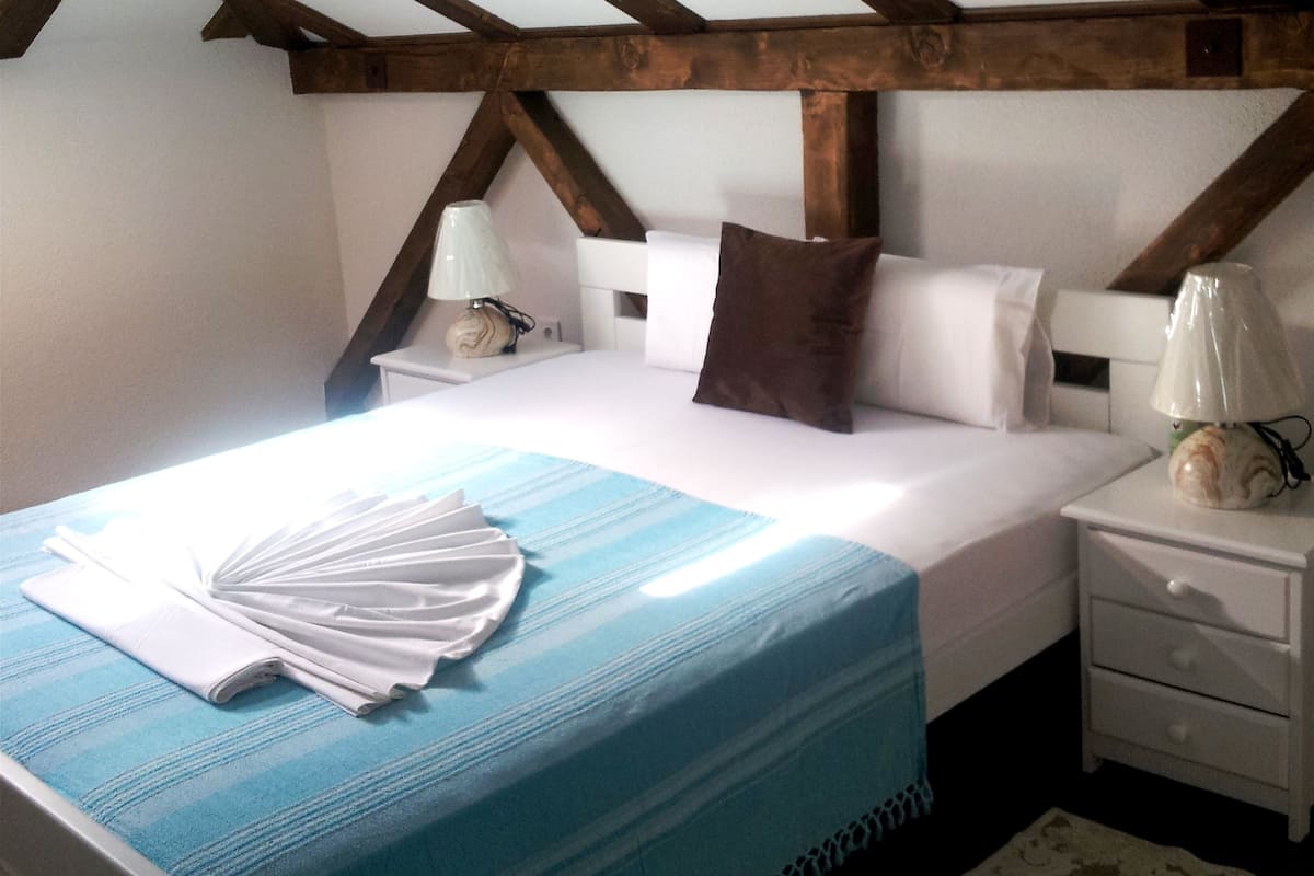 Un dormitorio con una cama, mesitas de noche blancas, una colcha azul y una alfombra estampada.