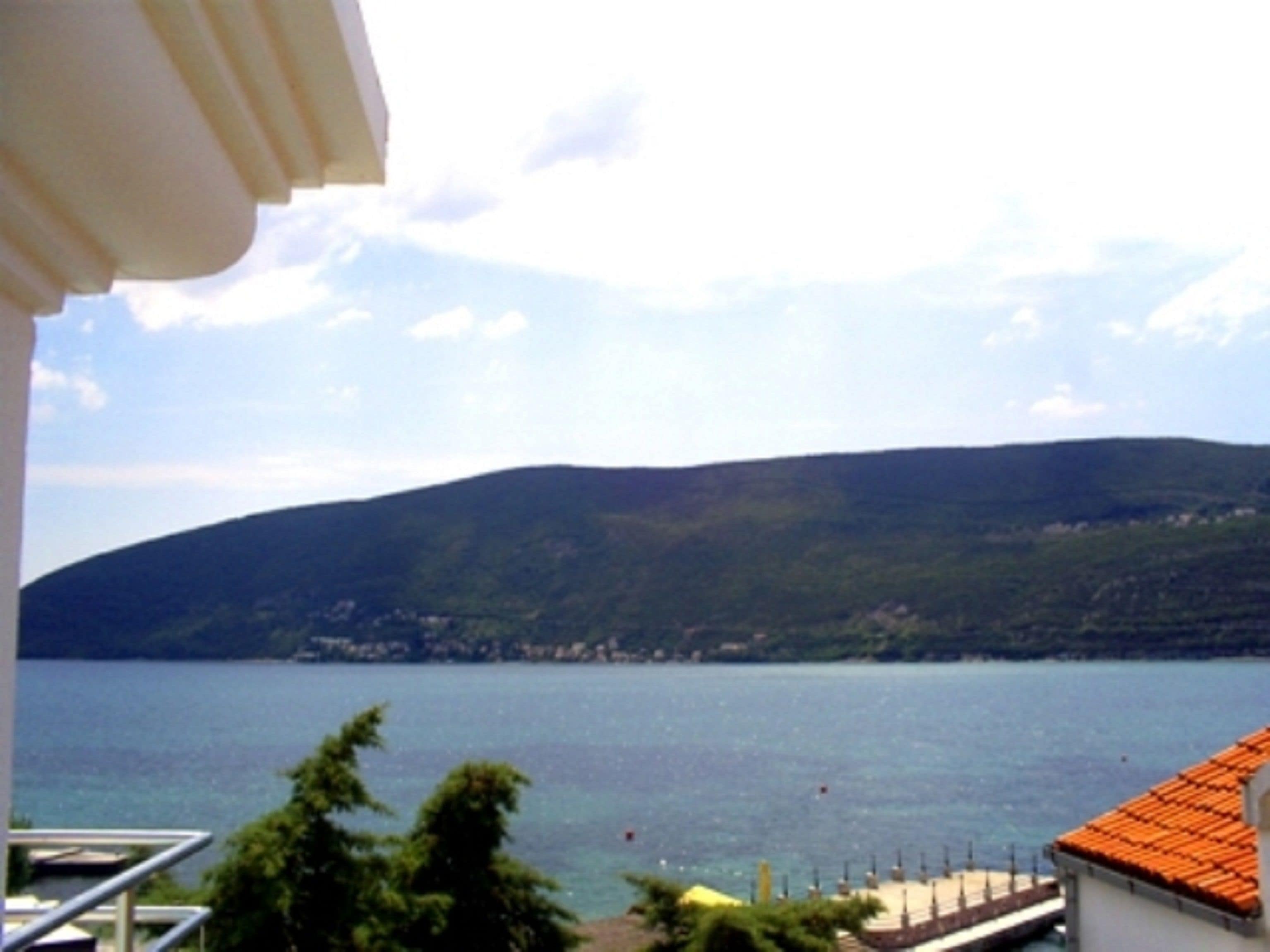 A coastal view with a mountain in the background, a body of water, and a building with a red-tiled roof.