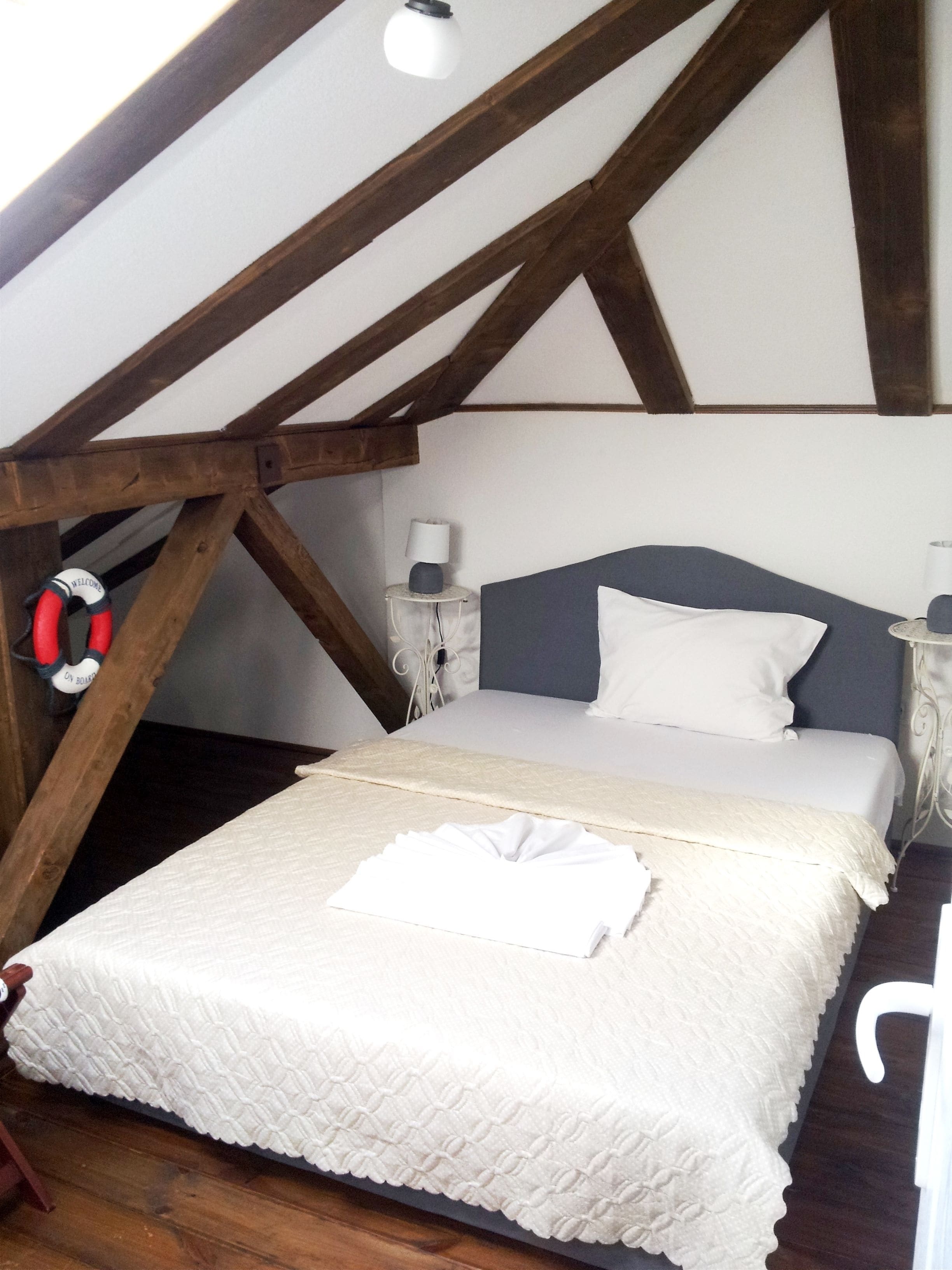 Un dormitorio con techo de madera, una cama con ropa de cama blanca, una mesita de noche con una lámpara y un cartel de bienvenida.
