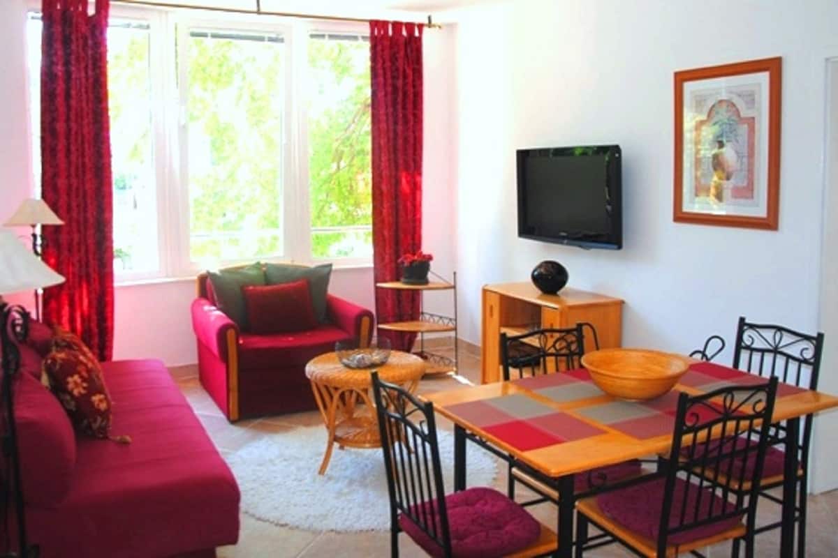 Una sala de estar acogedora con un sofá rojo, una mesita redonda y un televisor montado en la pared.