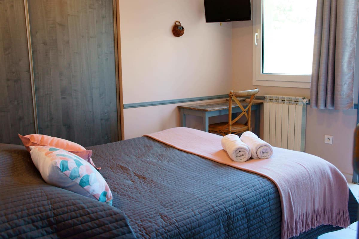 A bedroom with a bed, a small table, a radiator, and a television on the wall.