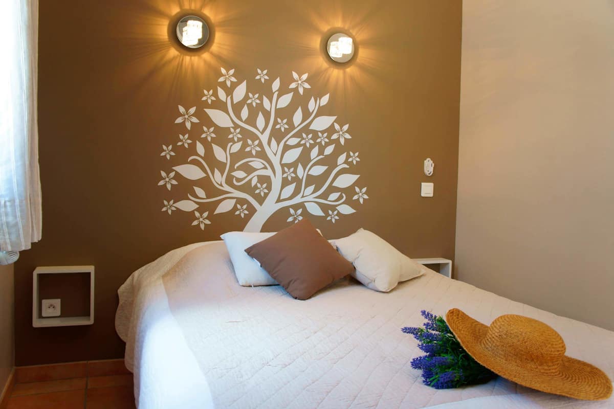 A neatly made bed with pillows, a wall-mounted light fixture, and a decorative wall decal.