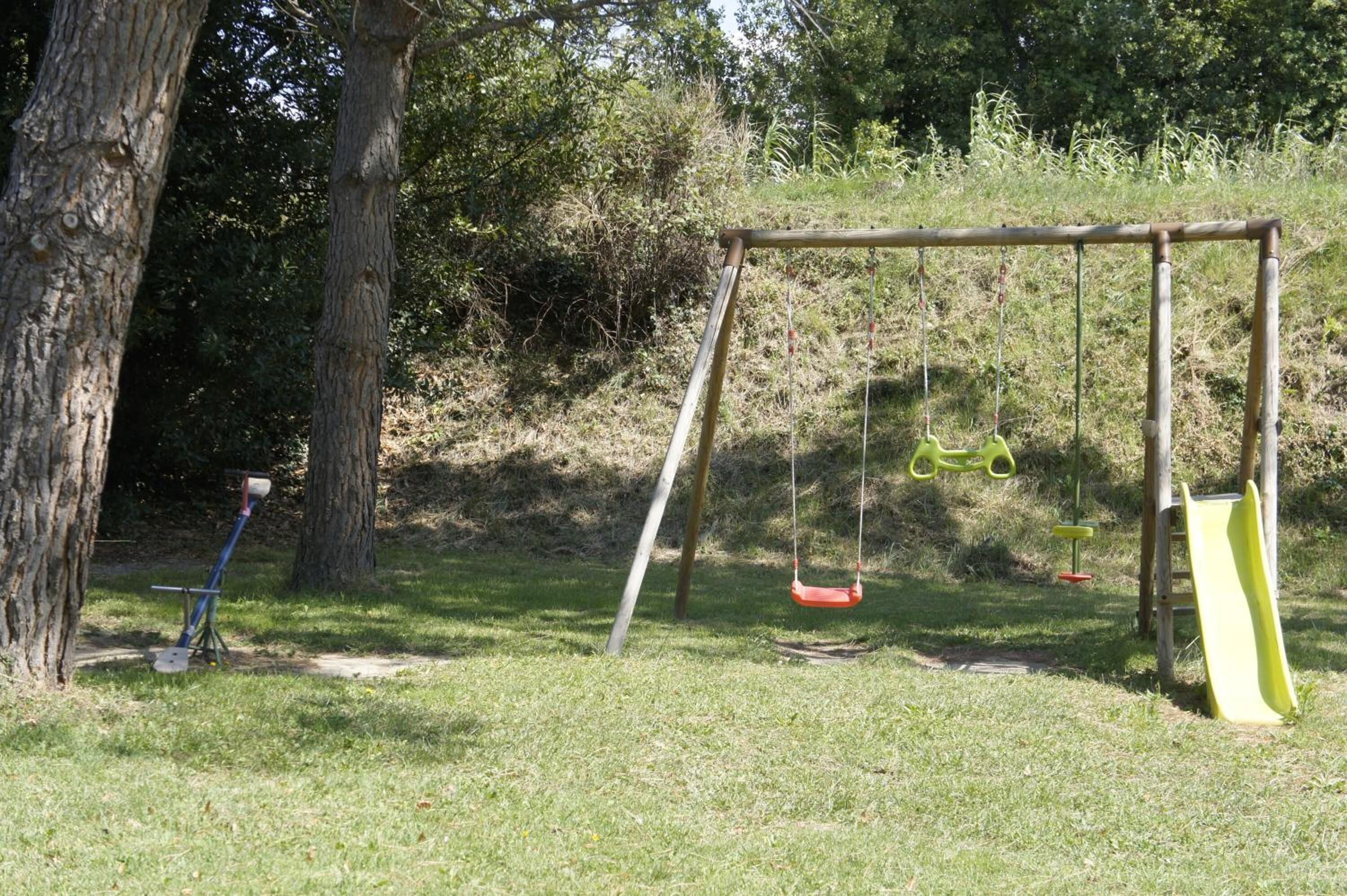 A playground with swings and a slide in a grassy area with trees.