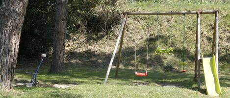 A playground with swings and a slide in a grassy area with trees.
