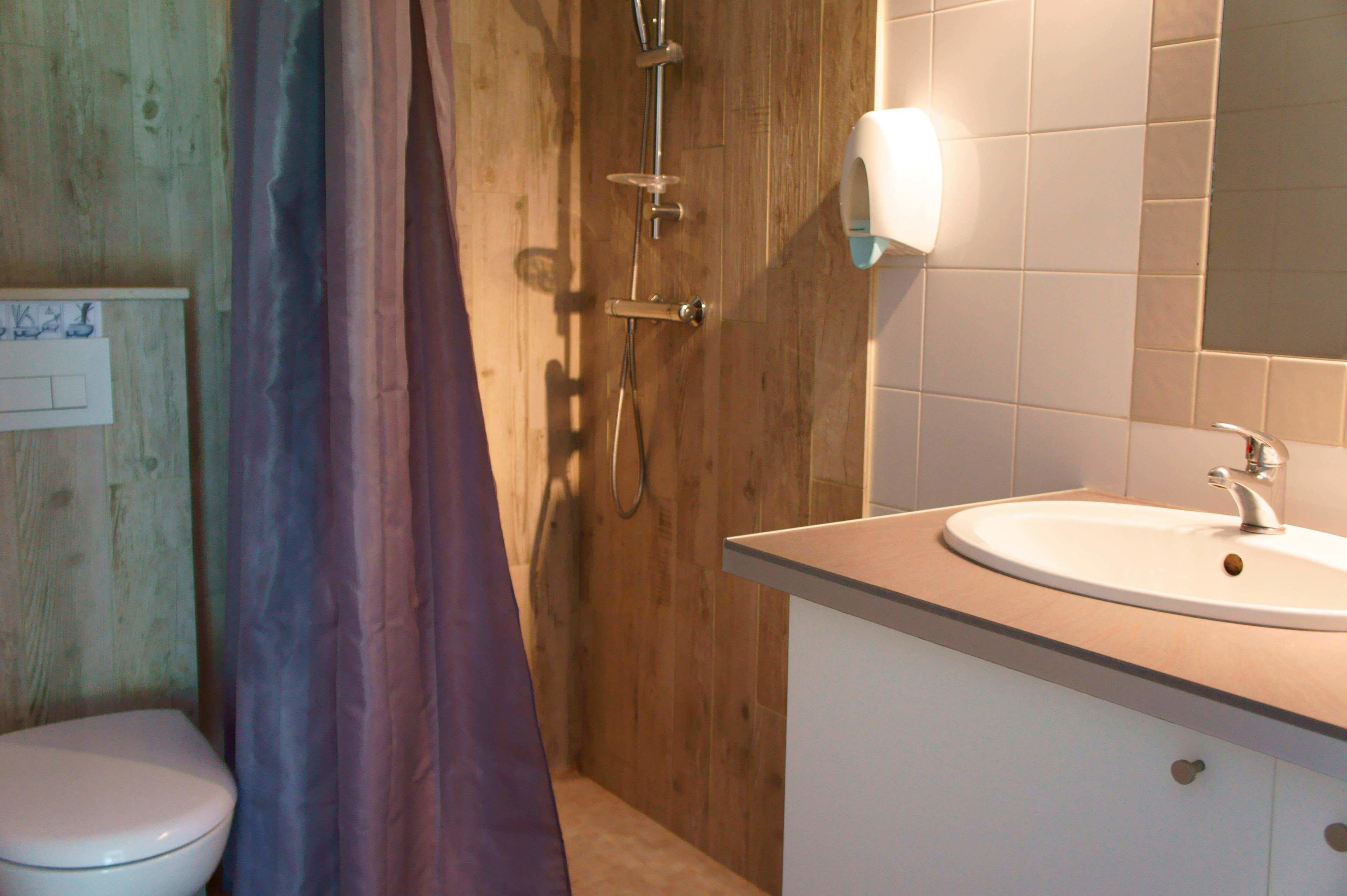 A bathroom with a wooden shower enclosure, a white sink with a mirror, and a toilet.