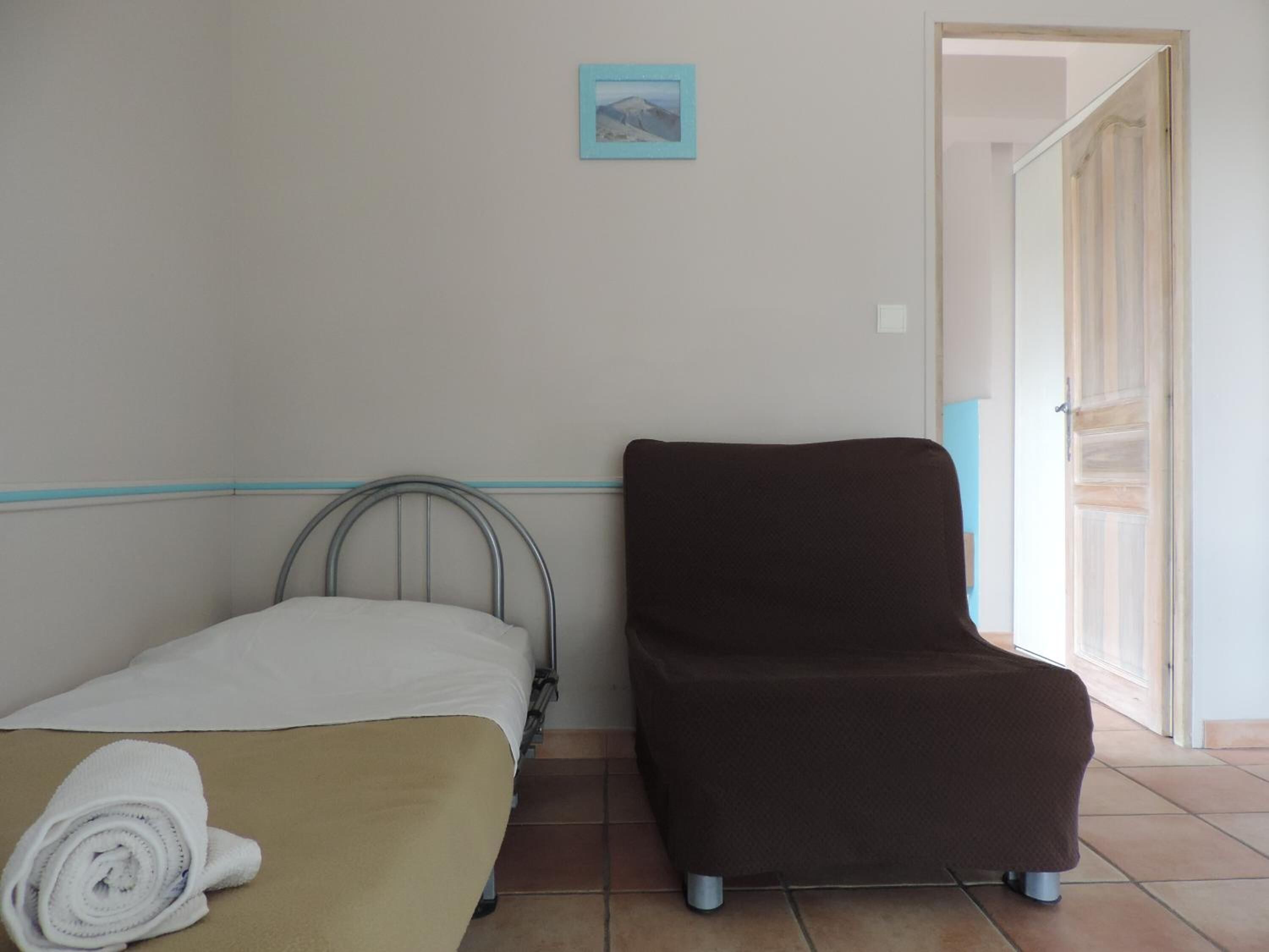 Una habitación con una cama, una silla marrón y un cuadro pequeño en la pared.
