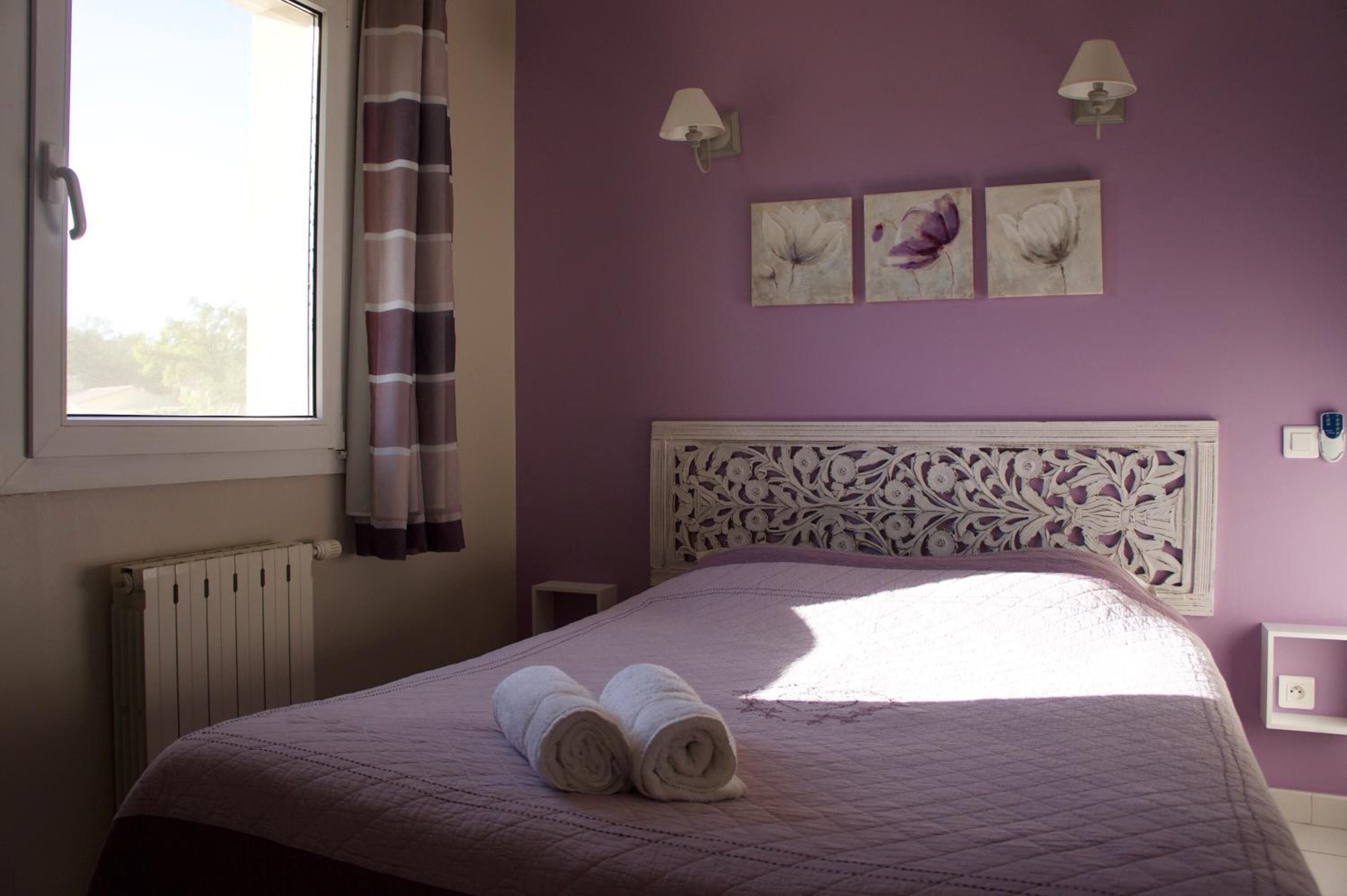A bedroom with a purple wall, a white headboard with floral patterns, and three wall-mounted lamps.